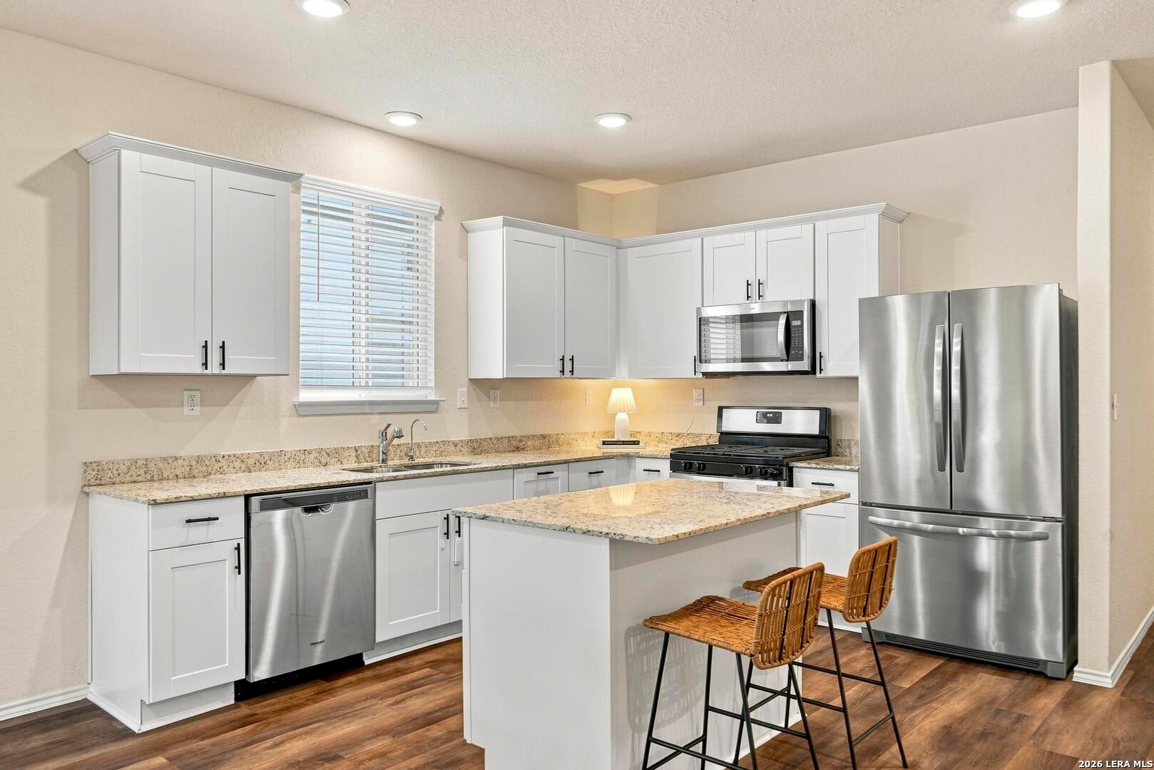 Kitchen with white cabinetry, granite counters, stainless appliances and center island